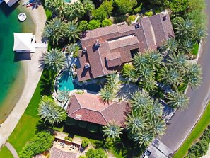 An aerial view of a property with multiple buildings, a swimming pool, and palm trees. - Lakefront home w/ beach + dock (Indio)
