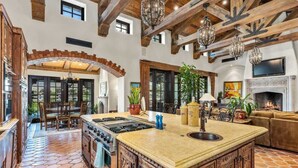 A spacious kitchen with a large island, wooden beams, and a fireplace. - Lakefront 6BR Estate | Private Beach, Pool & Dock (Indio)