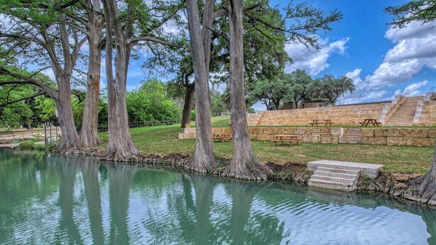 A tranquil outdoor setting with a pond, large trees, picnic tables, and stone steps leading to a viewing area. - Live Oak Cottage in Concan (Concan)