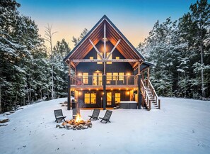Une cabane en rondins dotée d’un balcon, d’un foyer extérieur et d’un escalier menant à l’étage supérieur.