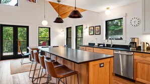 A modern kitchen with a large island, bar stools, a dishwasher, and a coffee maker.