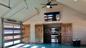 A spacious garage with a large door, a ceiling fan, and a kitchen area with appliances.