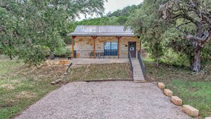A stone building with a metal roof, a covered patio, and a gravel driveway leading to a staircase.