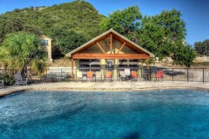 A pool area with a wooden deck, lounge chairs, and a covered seating area.