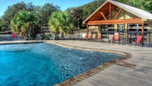 Ein Swimmingpool mit Holzterrasse und Liegestühlen, umgeben von Bäumen.