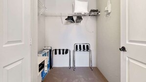 A small laundry room with a metal rack, a chair, and a shelf with folded clothes. - Old Town La Quinta | Pool-View Terrace + Hot tub (La Quinta)