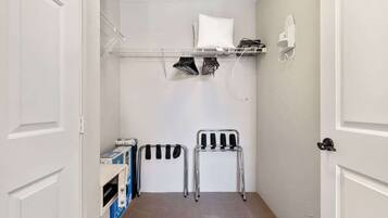 A small laundry room with a metal rack, a chair, and a shelf with folded clothes.