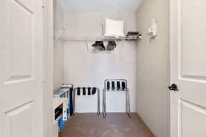 A small laundry room with a metal rack, a chair, and a shelf with folded clothes. - Old Town La Quinta | Pool-View Terrace + Hot tub (La Quinta)
