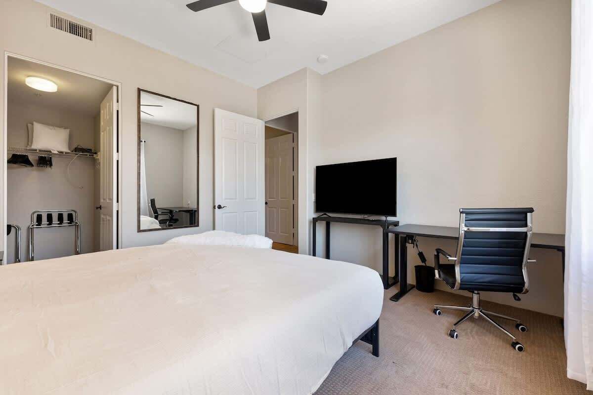 Et hotelværelse med en stor seng, et skrivebord med computer og fjernsyn, en stol og en ventilator.