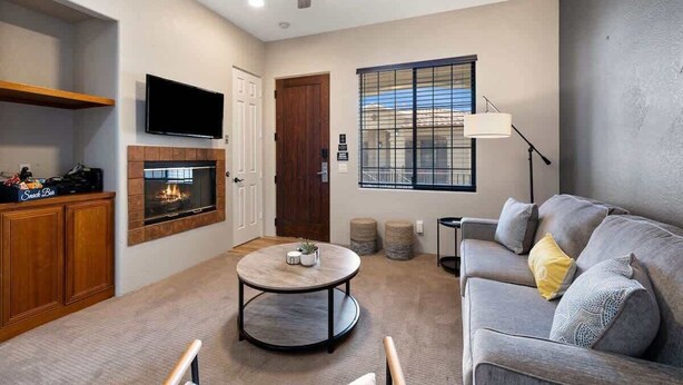 A living room with a fireplace, a sofa, a coffee table, a TV, and a ceiling fan. - Old Town La Quinta | Pool-View Terrace + Hot tub (La Quinta)