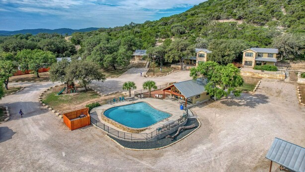 A resort with a swimming pool, a children's play area, and multiple buildings surrounded by greenery. - Oasis Home #3 on the Frio (Concan)
