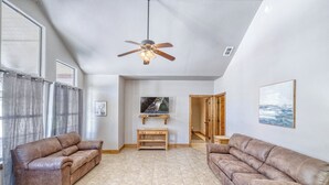 A spacious living room with two leather sofas, a ceiling fan, a flat-screen TV, and a wooden TV stand. - Oasis Home #3 on the Frio (Concan)