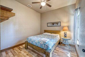 Ein Schlafzimmer mit einem hölzernen Bett, einem Deckenventilator, einem Nachttisch mit Lampe und einem fenster mit Vorhängen.