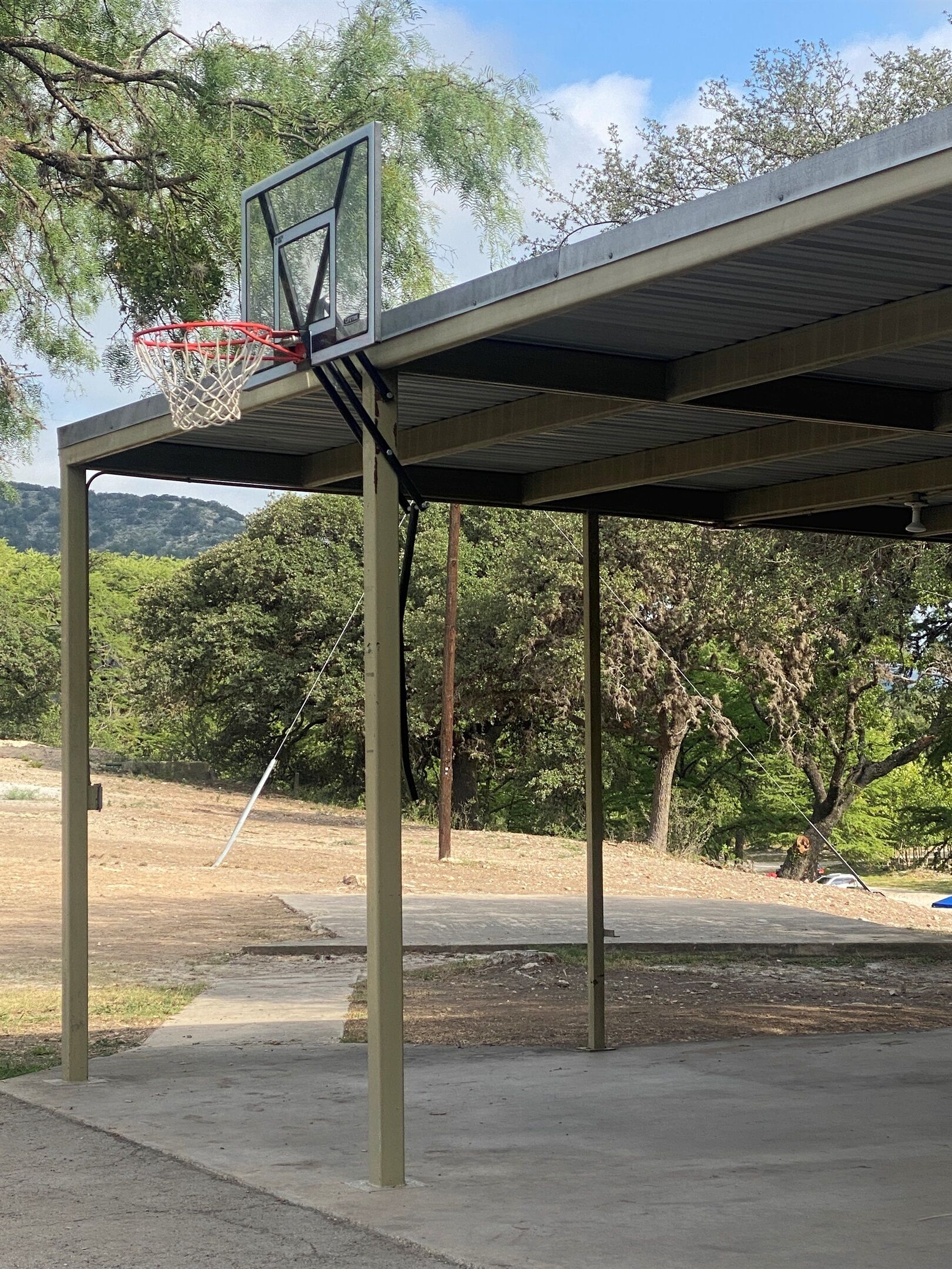 An outdoor basketball court with a metal roof and a basketball hoop.