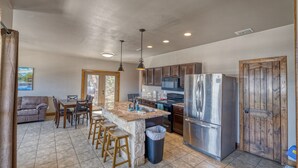 A spacious kitchen with a central island, stainless steel appliances, and wooden cabinets. - Oasis Lodge #2 on the Frio (Concan)