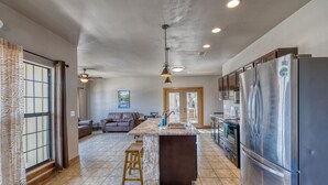 A spacious kitchen with a large island, stainless steel appliances, and a cozy living area with a sofa and a fireplace. - Oasis Lodge #2 on the Frio (Concan)