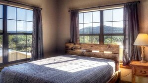 A bedroom with a large bed, wooden headboard, and a view of mountains through large windows.