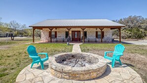A stone building with a covered patio, two Adirondack chairs, and a fire pit.