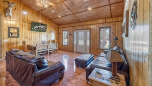 A wooden interior with a ceiling fan, a fireplace, leather sofas, and a dining area.
