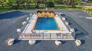 A square pool with a wooden deck and seating around it, surrounded by a fence and rocks.