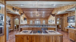 A spacious kitchen with wooden paneling, a central island with a stovetop, and deer antlers on the walls.