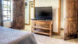 Quarto com uma cama, cômoda de madeira com televisão e um espelho grande.