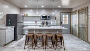 A kitchen with a central island, bar stools, a refrigerator, a microwave, and a sink. - River’s Edge Cabin #3 at Oasis Resort (Concan)