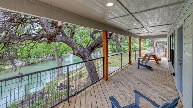 A covered deck with a view of a river and trees, wooden benches, and a picnic table. - River’s Edge Cabin #3 at Oasis Resort (Concan)