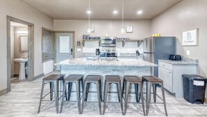 Una cocina moderna con una isla grande, taburetes de bar, electrodomésticos de acero inoxidable y vistas al baño contiguo.