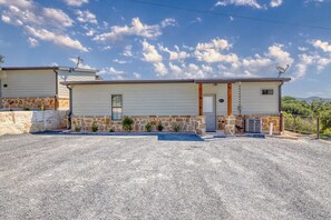 A two-story house with a stone foundation, a gravel driveway, and satellite dishes on the roof. - Rivers Edge Home #1 on the Frio (Concan)
