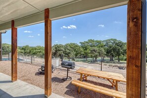 An outdoor patio with a wooden bench and grill, surrounded by a fence and trees. - Rivers Edge Home #1 on the Frio (Concan)