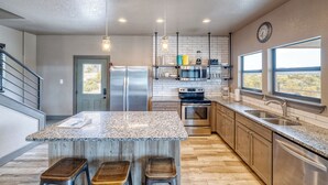 A modern kitchen with granite countertops, stainless steel appliances, and a large island with stools. - River's Edge Lodge #1 on the Frio (Concan)