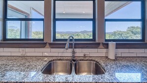 A kitchen with a double sink, large windows, and a view of a mountainous landscape. - River's Edge Lodge #2 on the Frio (Concan)