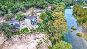 A modern house with a patio, a river, and surrounding greenery. - River's Edge Lodge #2 on the Frio (Concan)