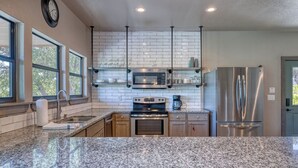 A modern kitchen with granite countertops, stainless steel appliances, and a large island. - River's Edge Lodge #3 on the Frio (Concan)