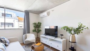 A modern living room with a sofa, a TV, a side table, and a potted plant.