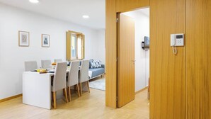 Een moderne, goed verlichte kamer met een eethoek, een bank en een houten deur met een telefoon.