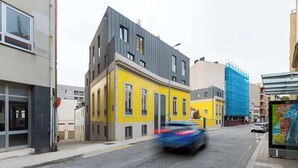 Straatbeeld met moderne gebouwen, waaronder een geel gebouw met een grijs dak en een blauw gebouw met steigerwerk.
