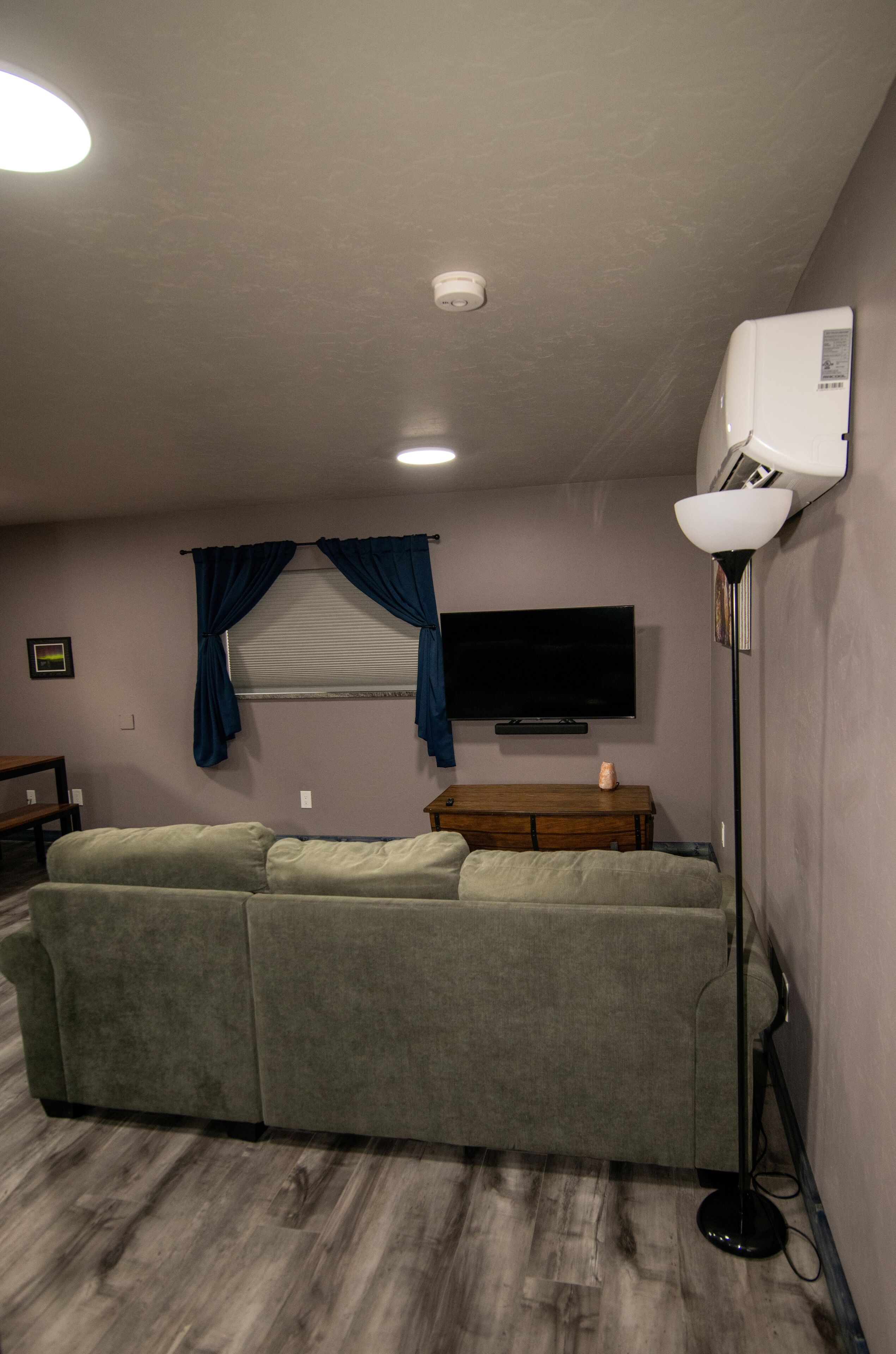 Ein Wohnzimmer mit einem Ecksofa, einem flachbildfernseher an der Wand, einem Deckenventilator und einer Stehlampe.