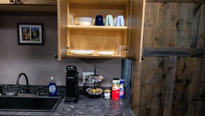 Een keuken met houten kastjes, een vaatwasser, en een aanrecht met een koffiezetapparaat, potten en een afwasschaal.