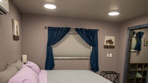 Een slaapkamer met een bed, een dressoir, een spiegel en een raam met gordijnen.