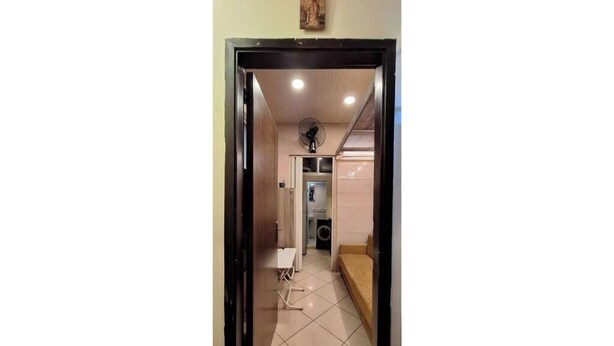 Un corridoio che conduce a una zona cucina con una ventola, una lavatrice e un divano.