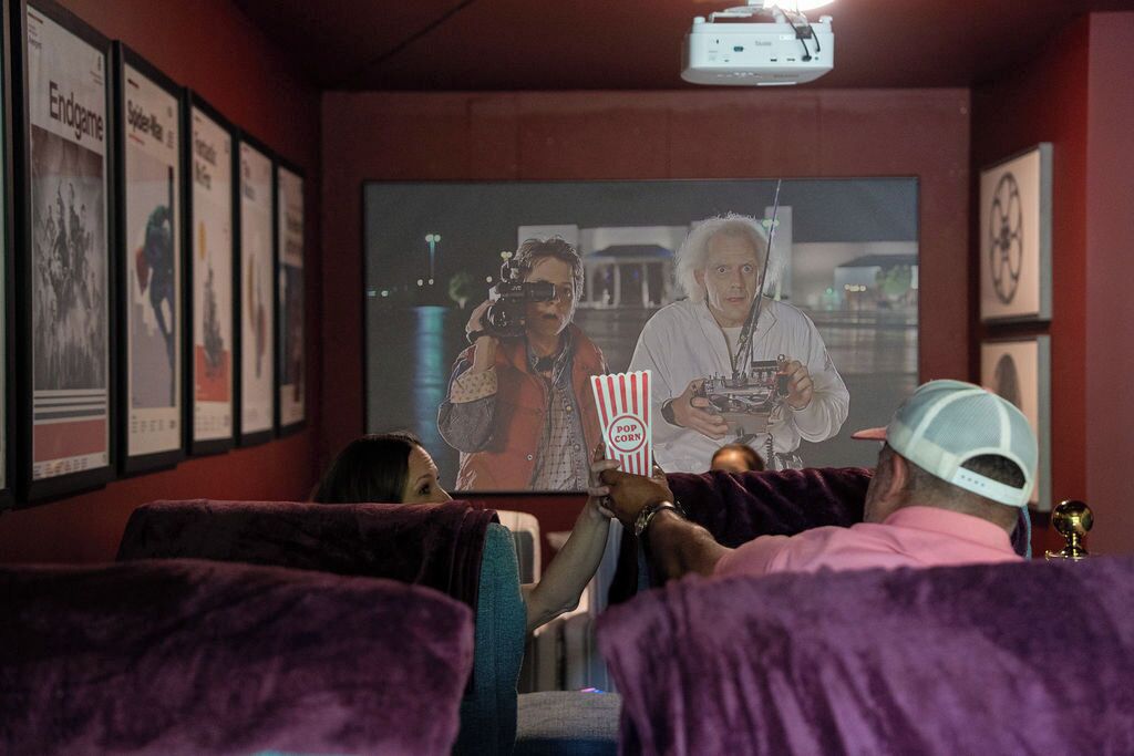 Un cine con paredes rojas, carteles en las paredes y gente viendo una película.