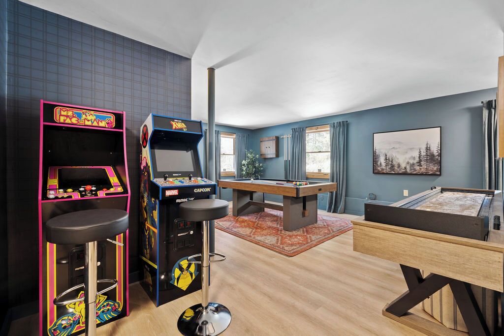 A room with a pool table, arcade machines, and a bar stool.