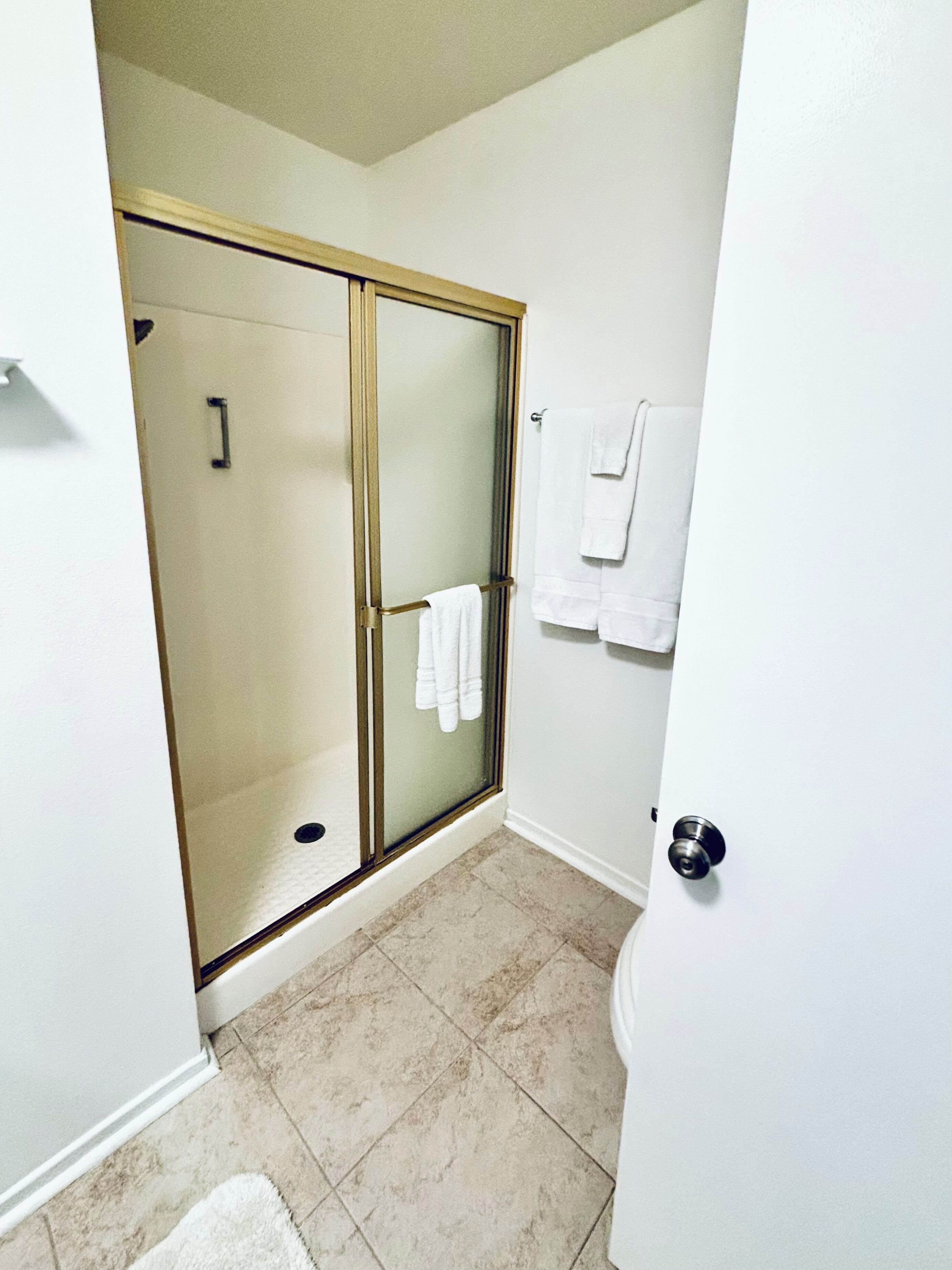A bathroom with a glass-enclosed shower, white tiles, and a towel rack with towels.