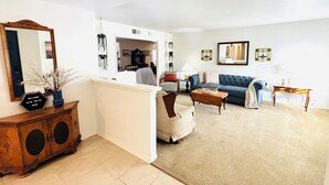 A living room with a sofa, a coffee table, a side table, and a mirror. There is a cabinet with a sign on top.