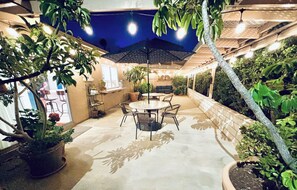 An outdoor patio with a round table and chairs, surrounded by potted plants and a large umbrella. - Walk to Lagoon/6 minutes from Legoland/Golfers Destination (Carlsbad)