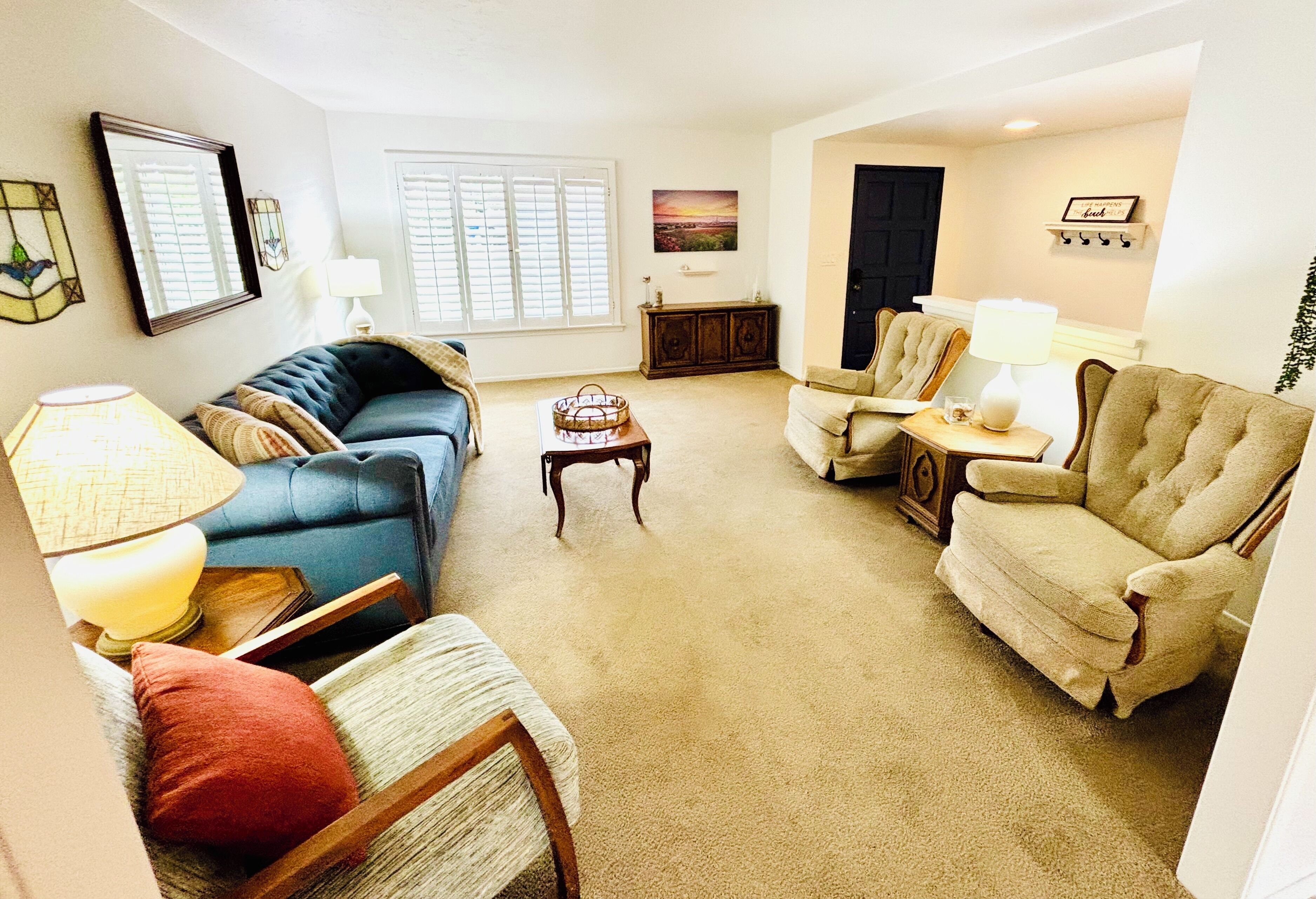 A living room with a blue sofa, beige armchairs, a wooden coffee table, and a lamp.