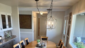 Un coin repas comprenant une table ronde en bois, six chaises, un comptoir en granit et un luminaire suspendu.