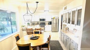 Une cuisine moderne avec des armoires blanches, des appareils en acier inoxydable et un coin repas comprenant une table et des chaises en bois.